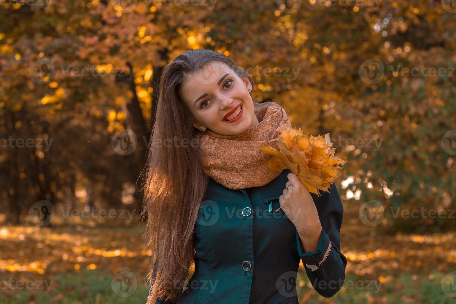 hermosa chica alegre con cabello largo y una cálida bufanda mantiene sus hojas en su mano sonríe foto