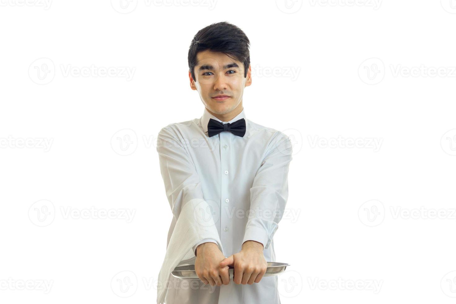guapo joven camarero sonríe se pone de pie y sostiene una bandeja foto