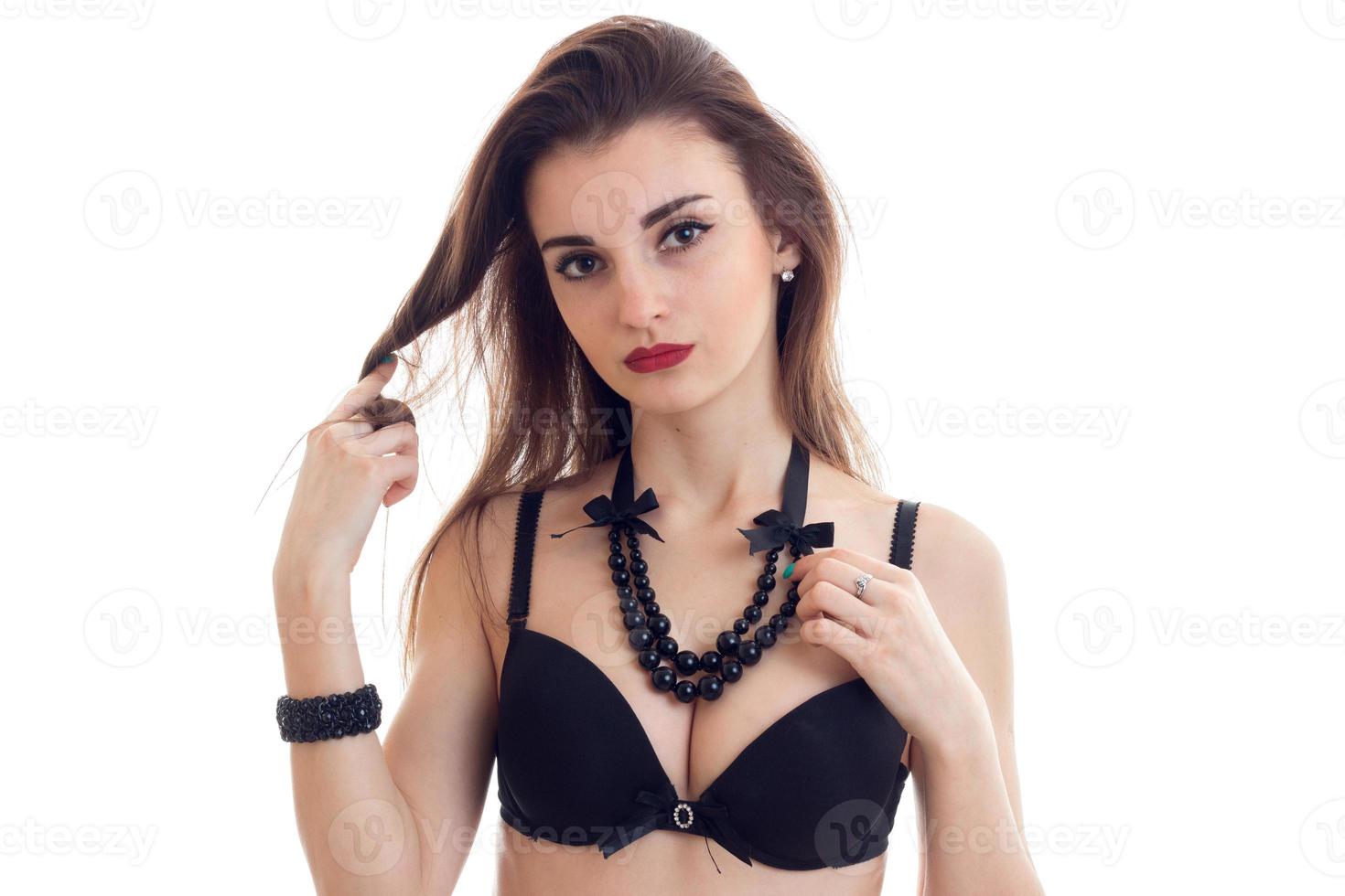 beautiful young brunette with red lipstick with big breasts in a black bra with beads around her neck looks into the camera photo