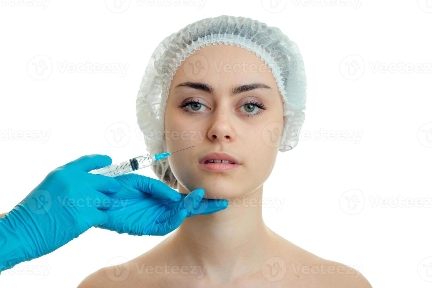 retrato de primer plano de una niña con una gorra médica en el médico que le hace el pinchazo en la cara foto