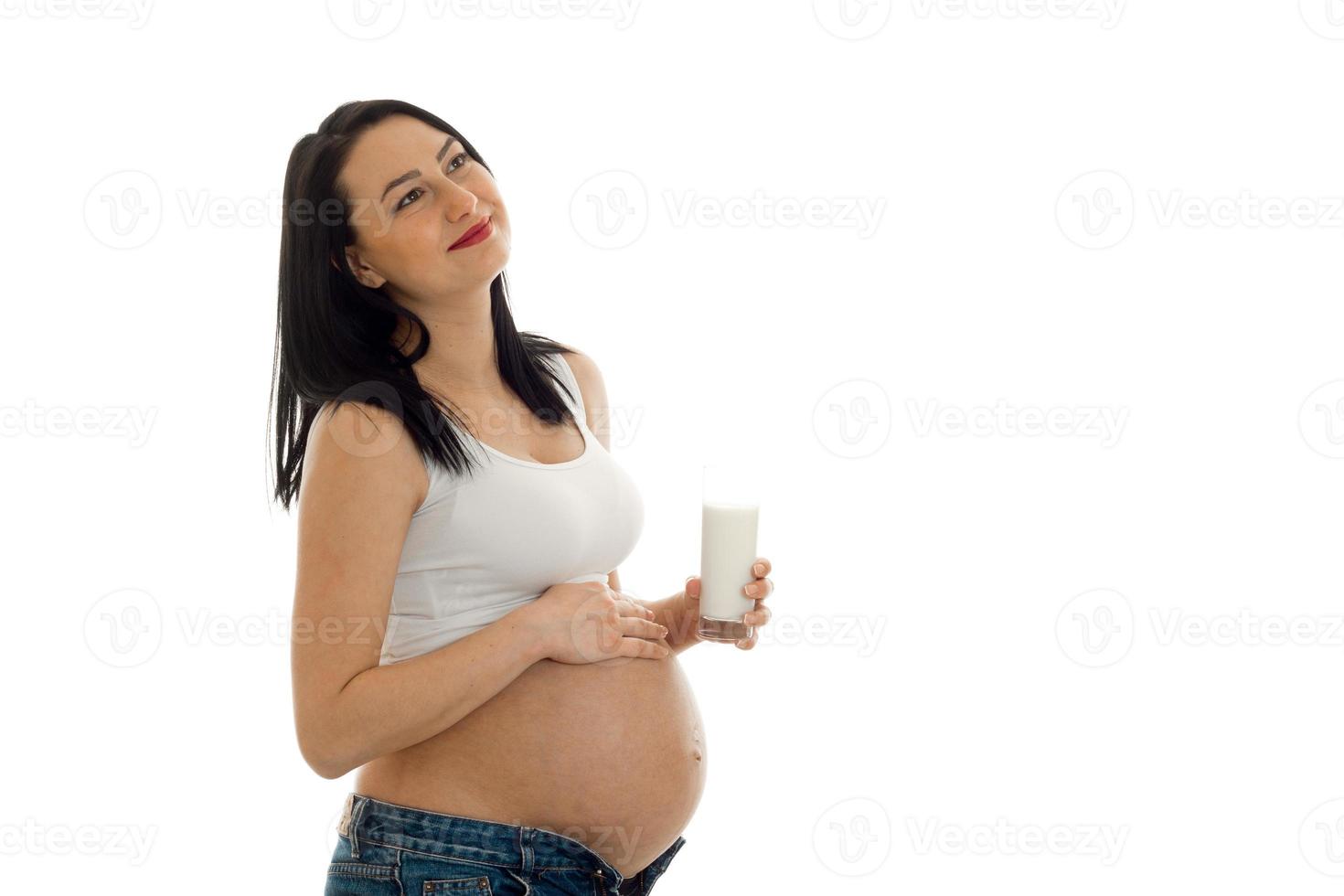 charming young brunette pregnant girl with glasses of milk and hand on her belly posing isolated on white background photo