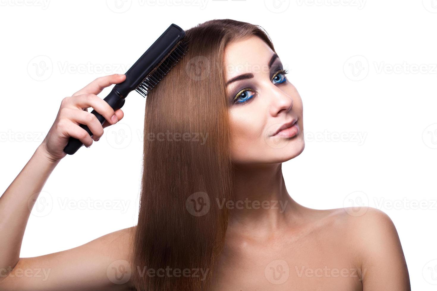 chica voluptuosa con ojos azules peinando su perfecto cabello castaño sano con peine sobre fondo blanco foto