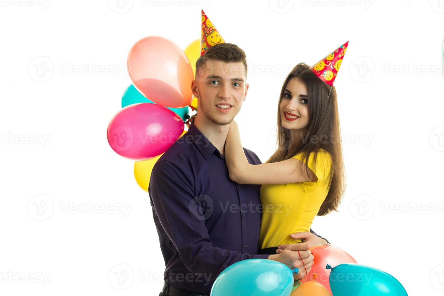 joven pareja gay de pie uno al lado del otro con grandes globos de colores y sombreros en forma de cono en la cabeza foto
