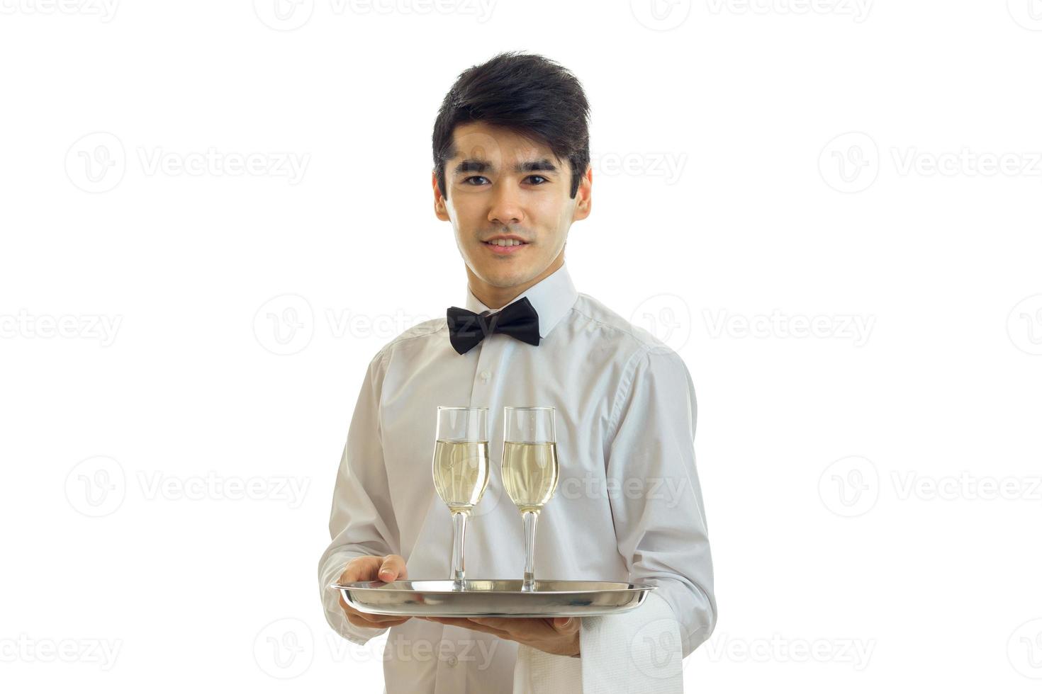 camarero encantador con una camisa blanca sosteniendo una bandeja con vasos de alcohol foto