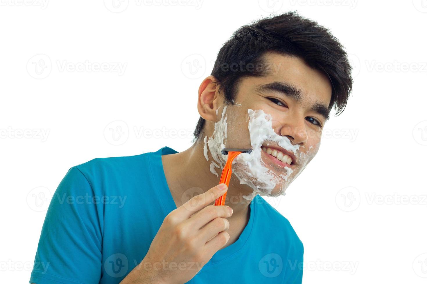 hermoso tipo sonriente con espuma en la cara mira a la cámara y se afeita la barba foto