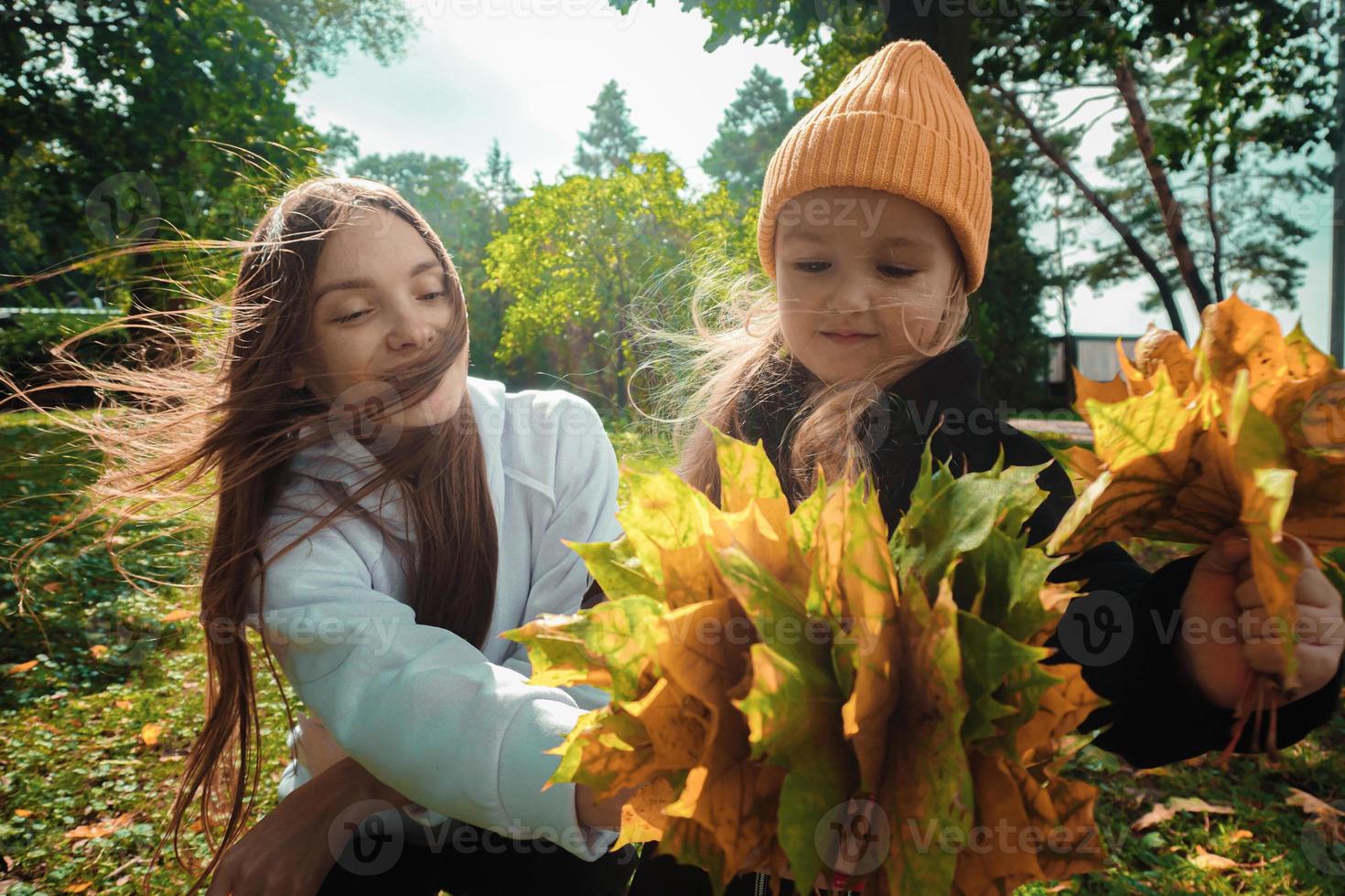 madre con hija recoge un ramo de hojas de otoño en el parque foto