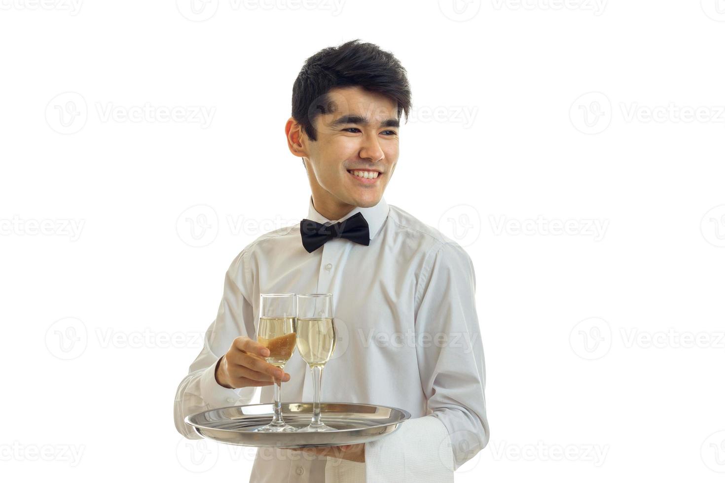 Hilarious cute young waiter looks away laughing and holding wine glasses on a tray that photo