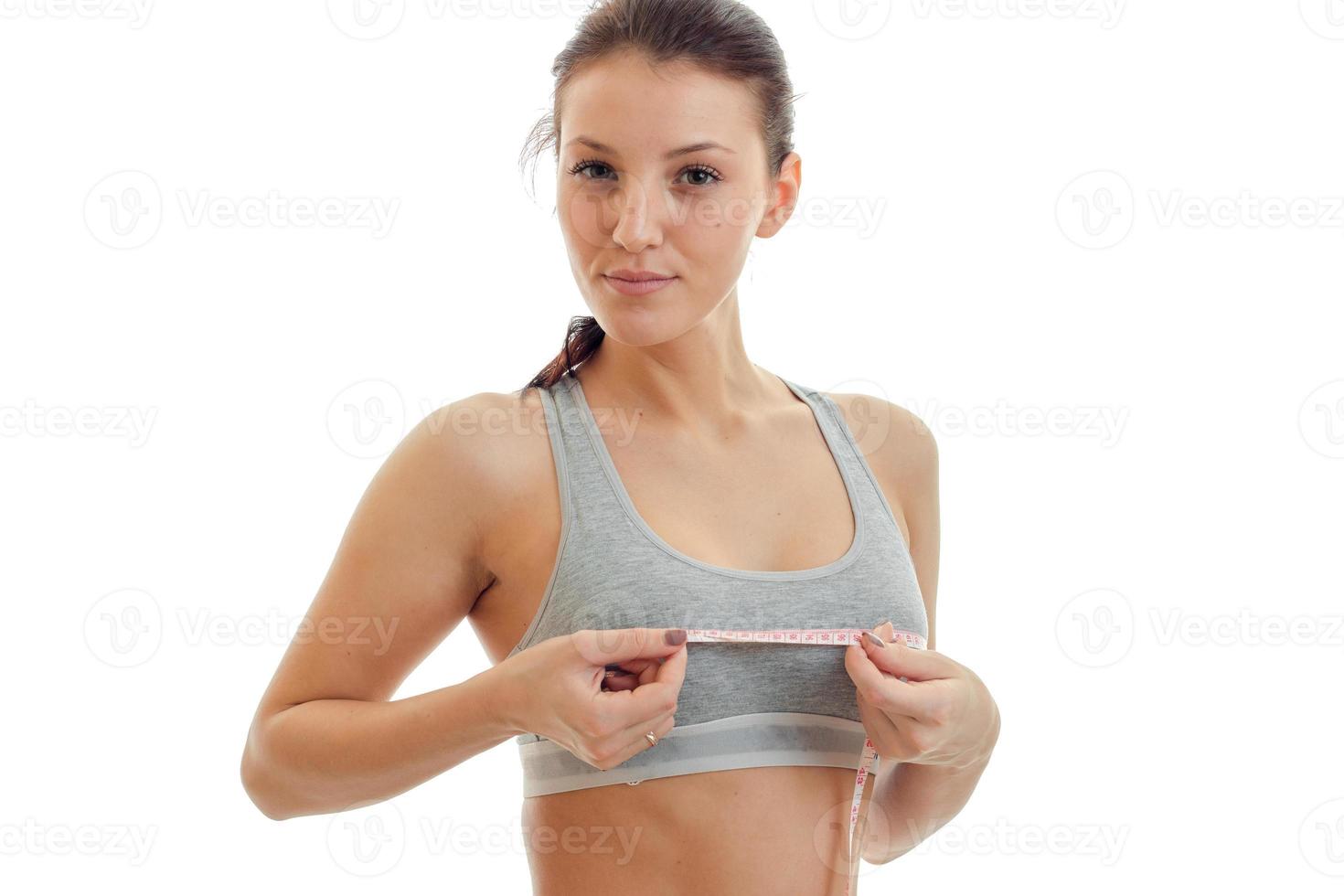beautiful young girl in grey top looks into the camera and takes the measuring tape chest close-up photo