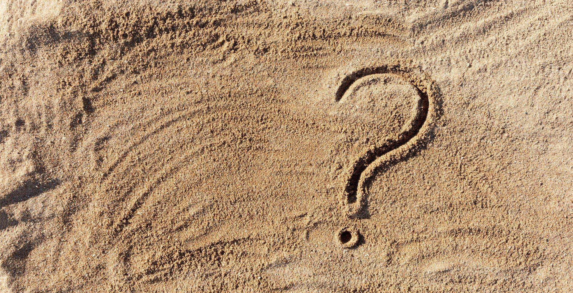 question marks written on beach sand close up, with copy space photo