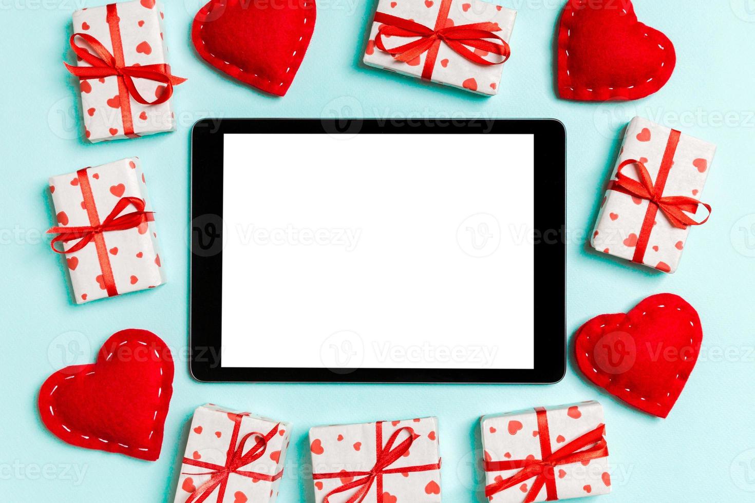 Top view of digital tablet surrounded with gift boxes and hearts on colorful background. Saint Valentine's day photo