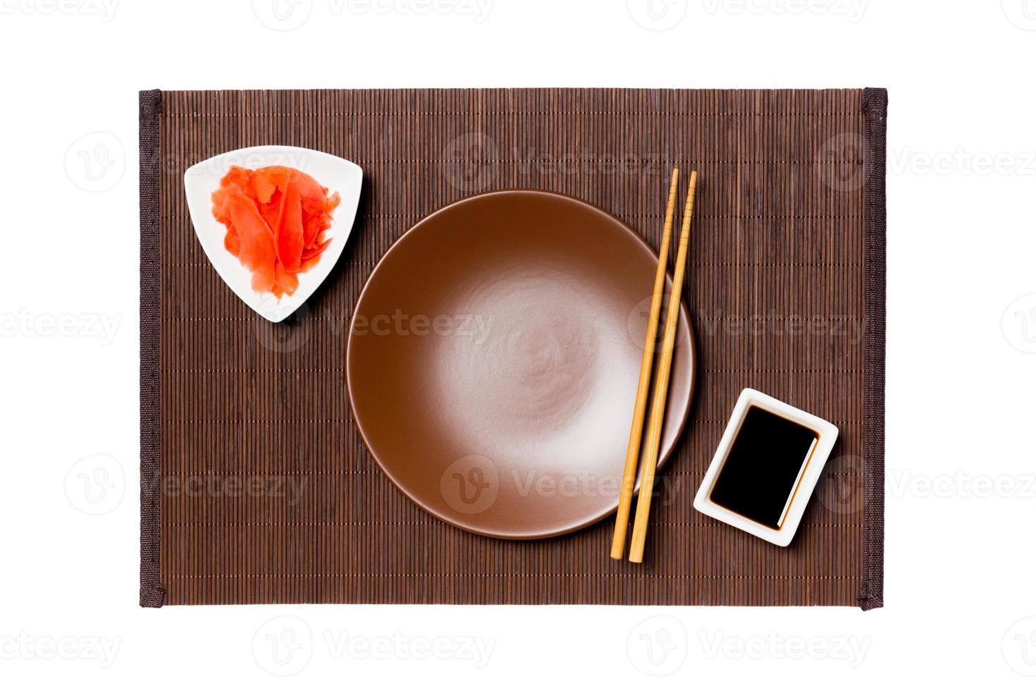 Empty round brown plate with chopsticks for sushi, ginger and soy sauce on dark bamboo mat background. Top view with copy space for you design photo