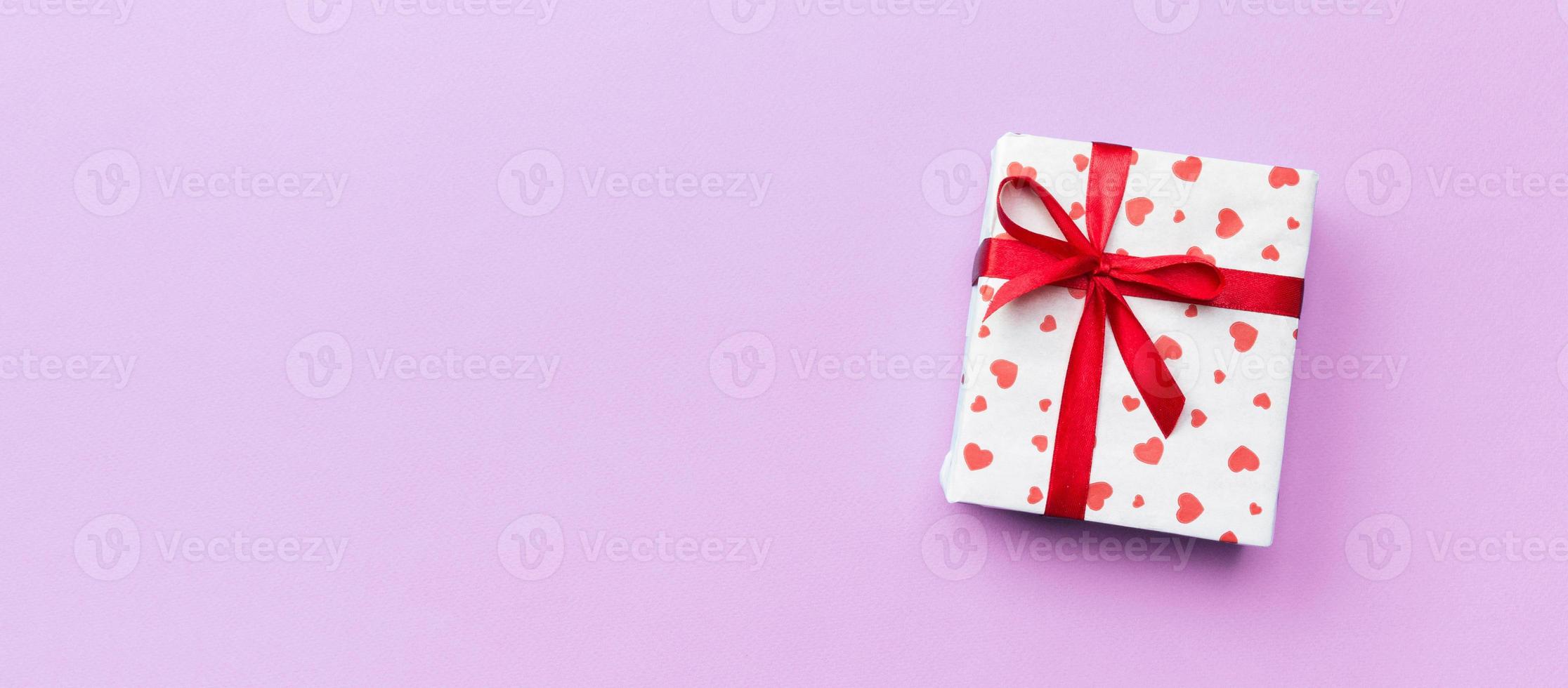 Valentine or other holiday handmade present in paper with red hearts and gifts box in holiday wrapper. Present box of gift on violet colored table top view with copy space, empty space for design photo