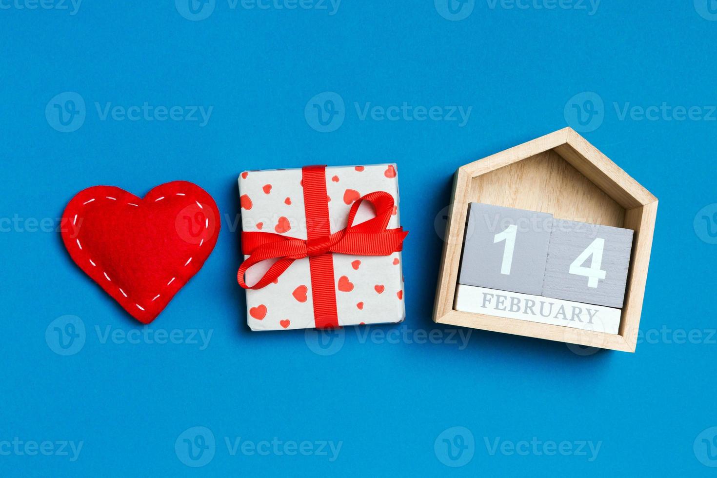 Composition of wooden calendar, holiday white gift boxes and red textile hearts on colorful background. The fourteenth of February. Valentine's day concept photo