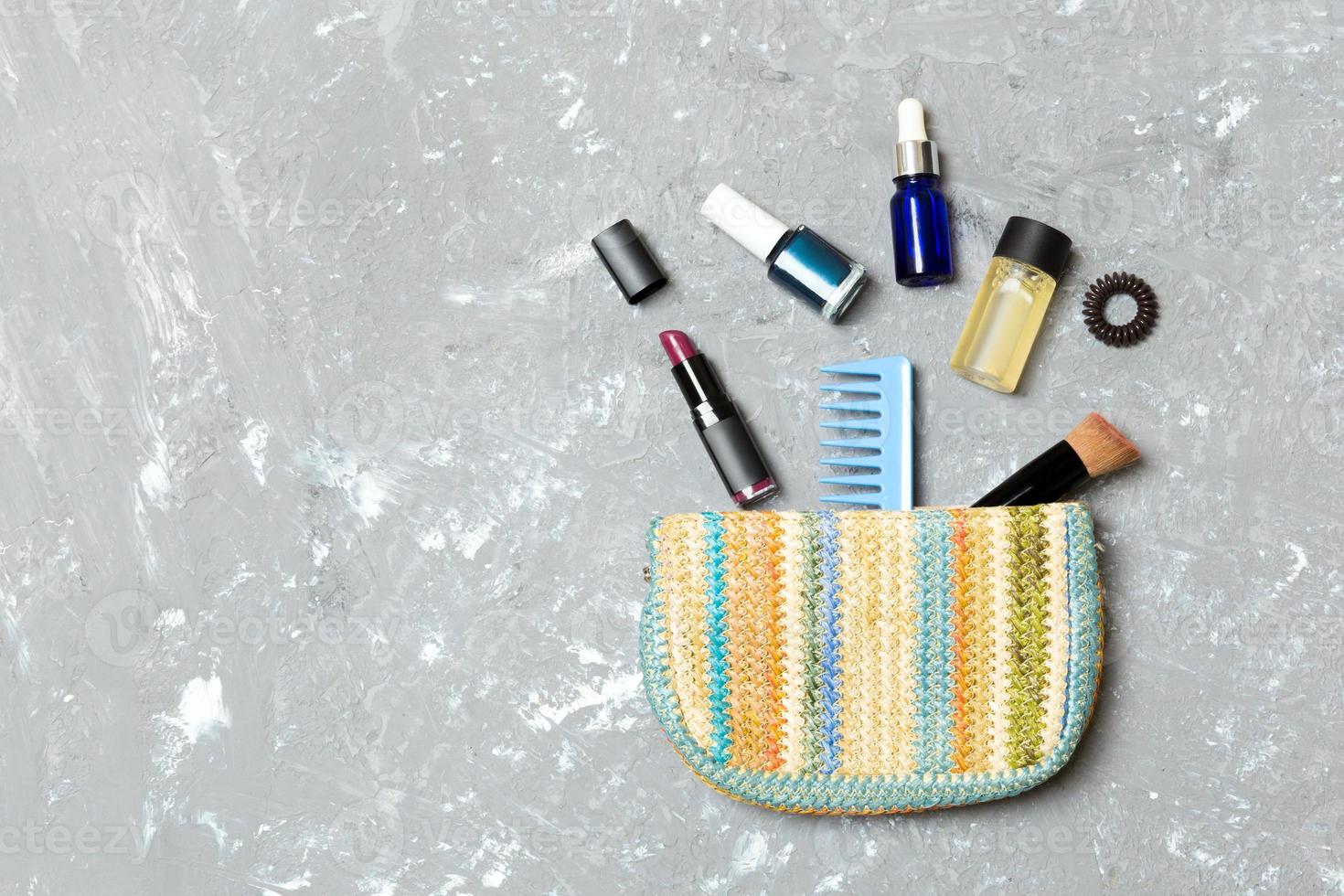 Make up products spilling out of cosmetics bag on grey cement background with empty space for your design photo