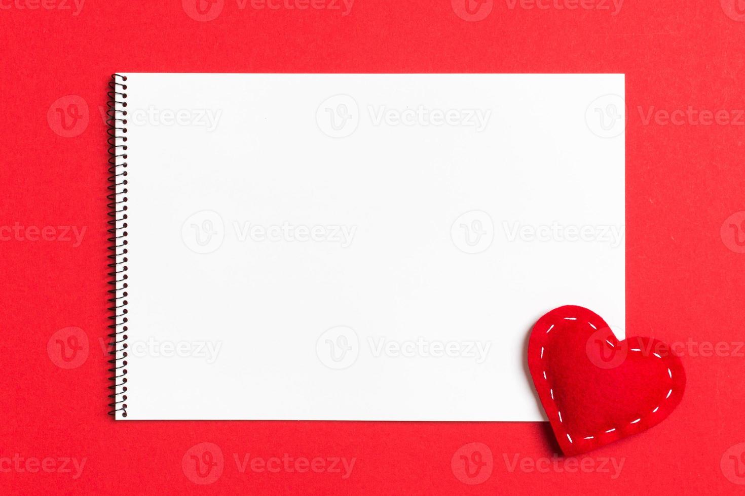 Top view of notebook surrounded with a textile heart on colorful background. Valentine's Day concept photo