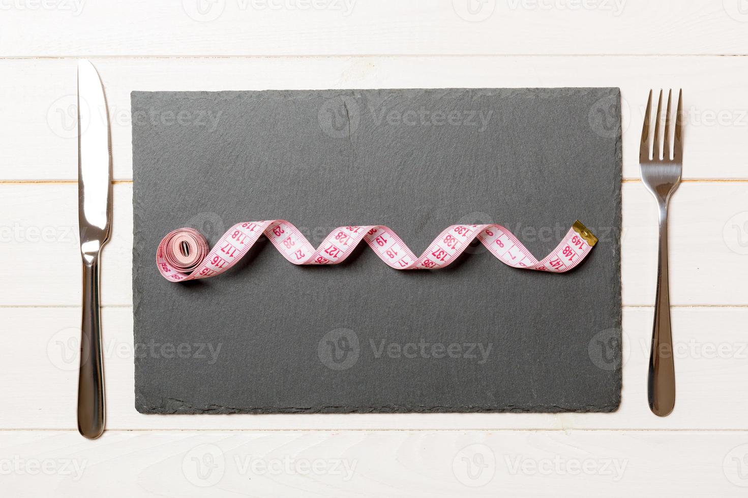 Healthy diet concept of plate with measuring tape, fork and knife on wooden background. Top view photo
