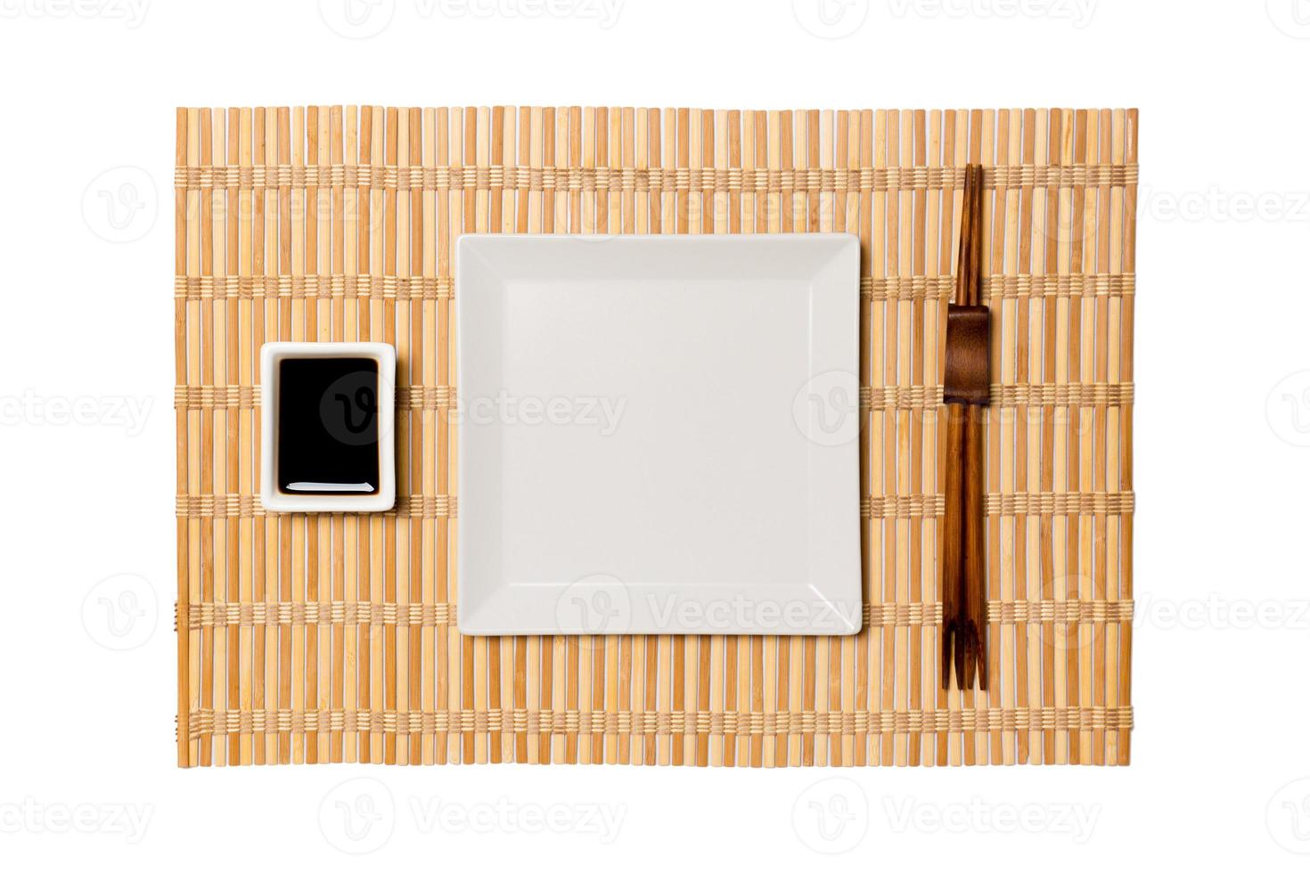 Empty white square plate with chopsticks for sushi and soy sauce on yellow bamboo mat background. Top view with copy space for you design photo