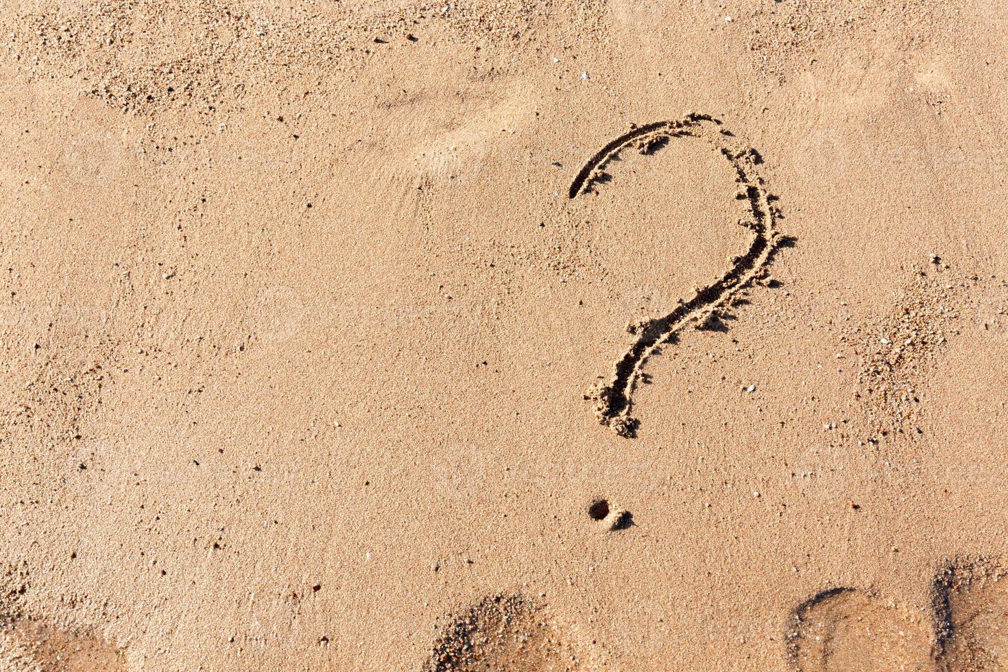 Question mark sign on sand beach near the sea. Concept of dilemma, answer and question photo