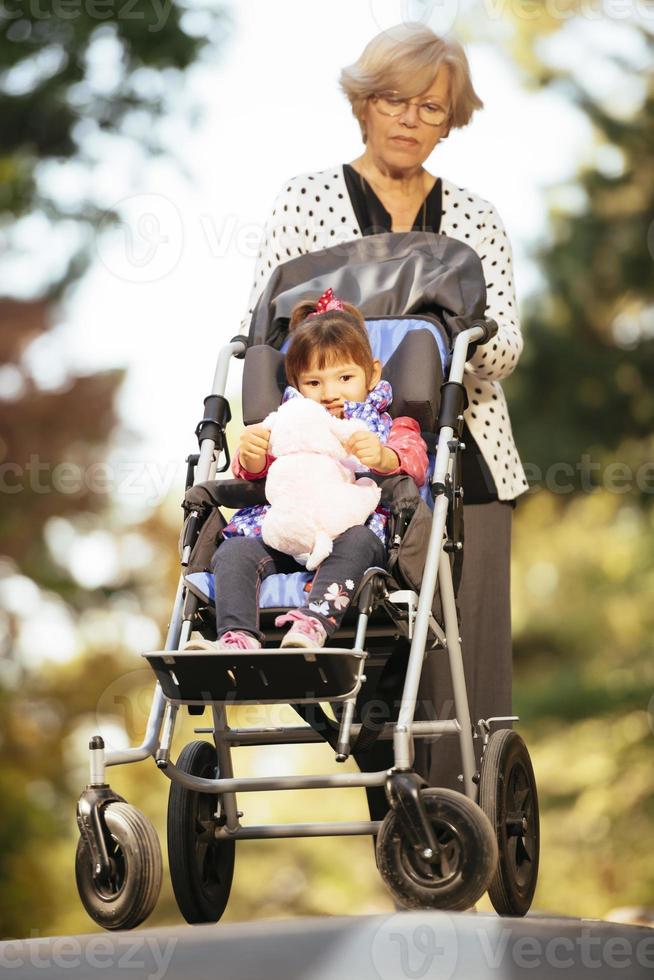 Grandmother and her autistic grand daughter enjoying holiday together outdoors, lying on green grass on blanket and smiling to camera. Leisure family lifestyle, happiness and moments. photo