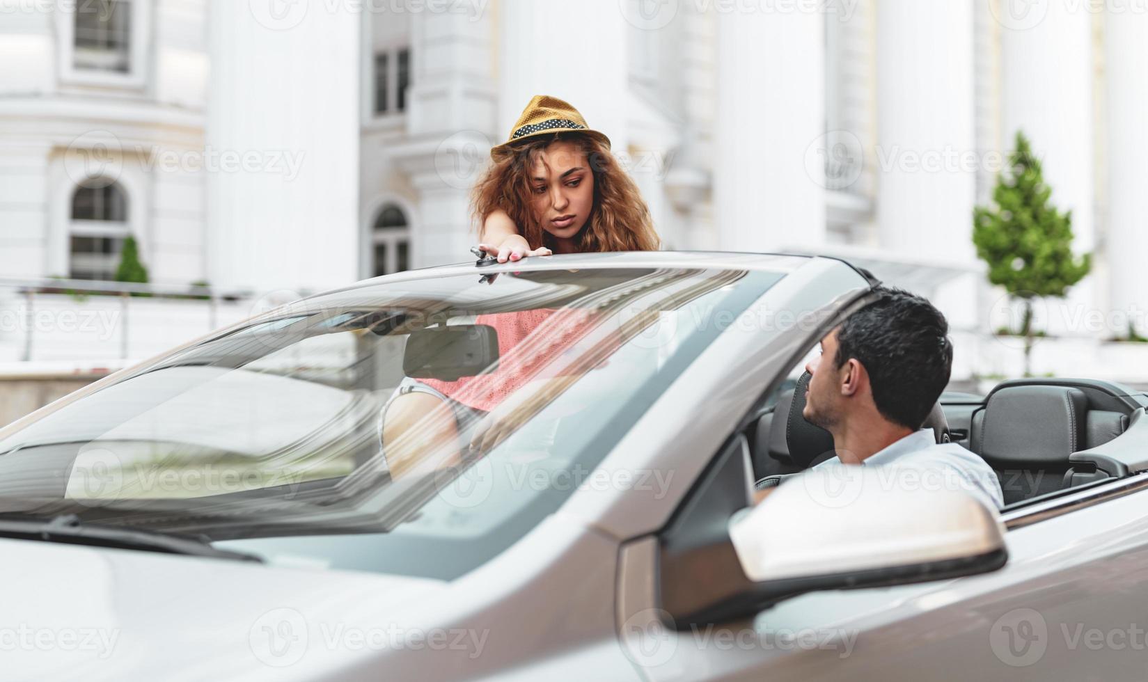 Friends having fun at car trip around the world. Couple in love with arms up on a convertible car. photo