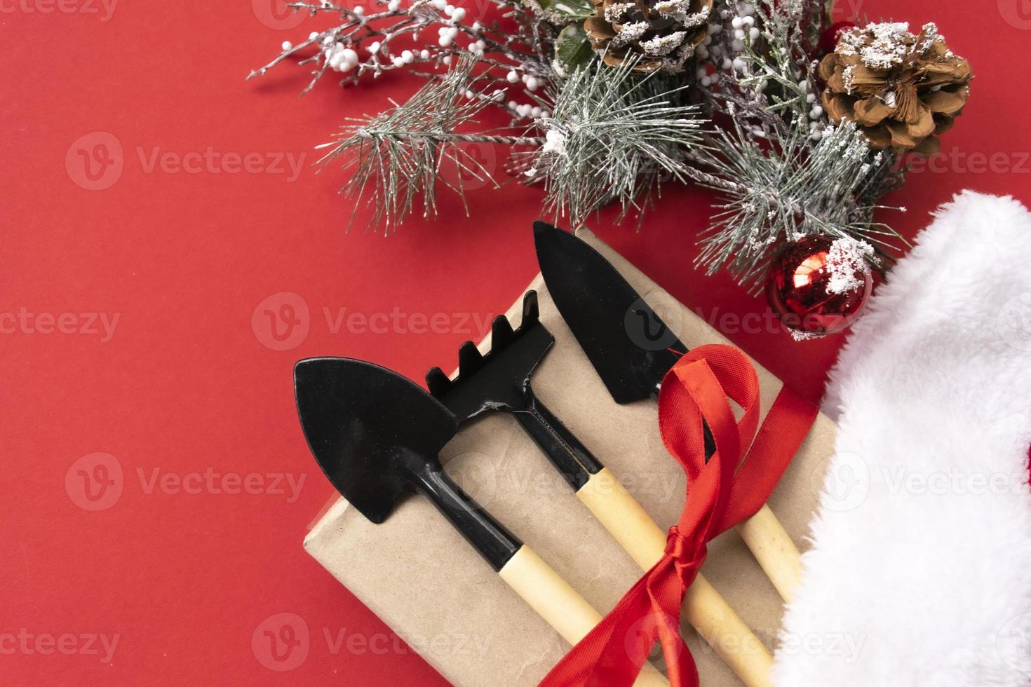 Christmas and new year composition with garden tools, shovel and rake and Santa Claus hat on a red background. The concept of gardening and farming for cards, calendars, covers. photo