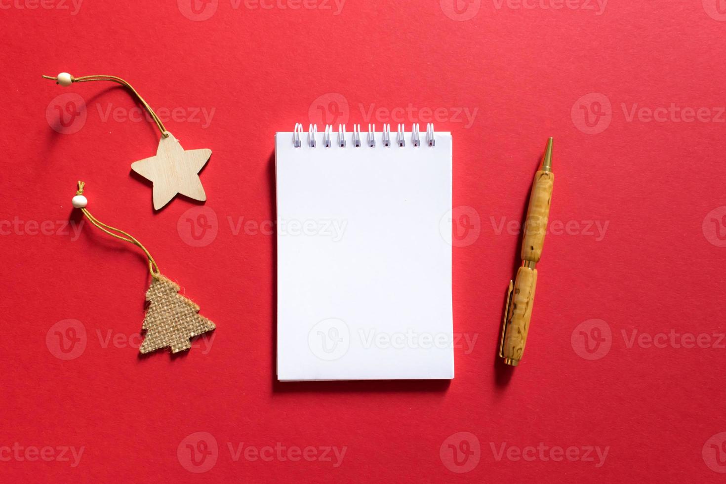 Notebook and pen on a red background, spiral notepad with christmas tree and star on a table. space for your text, greetings, top view. photo