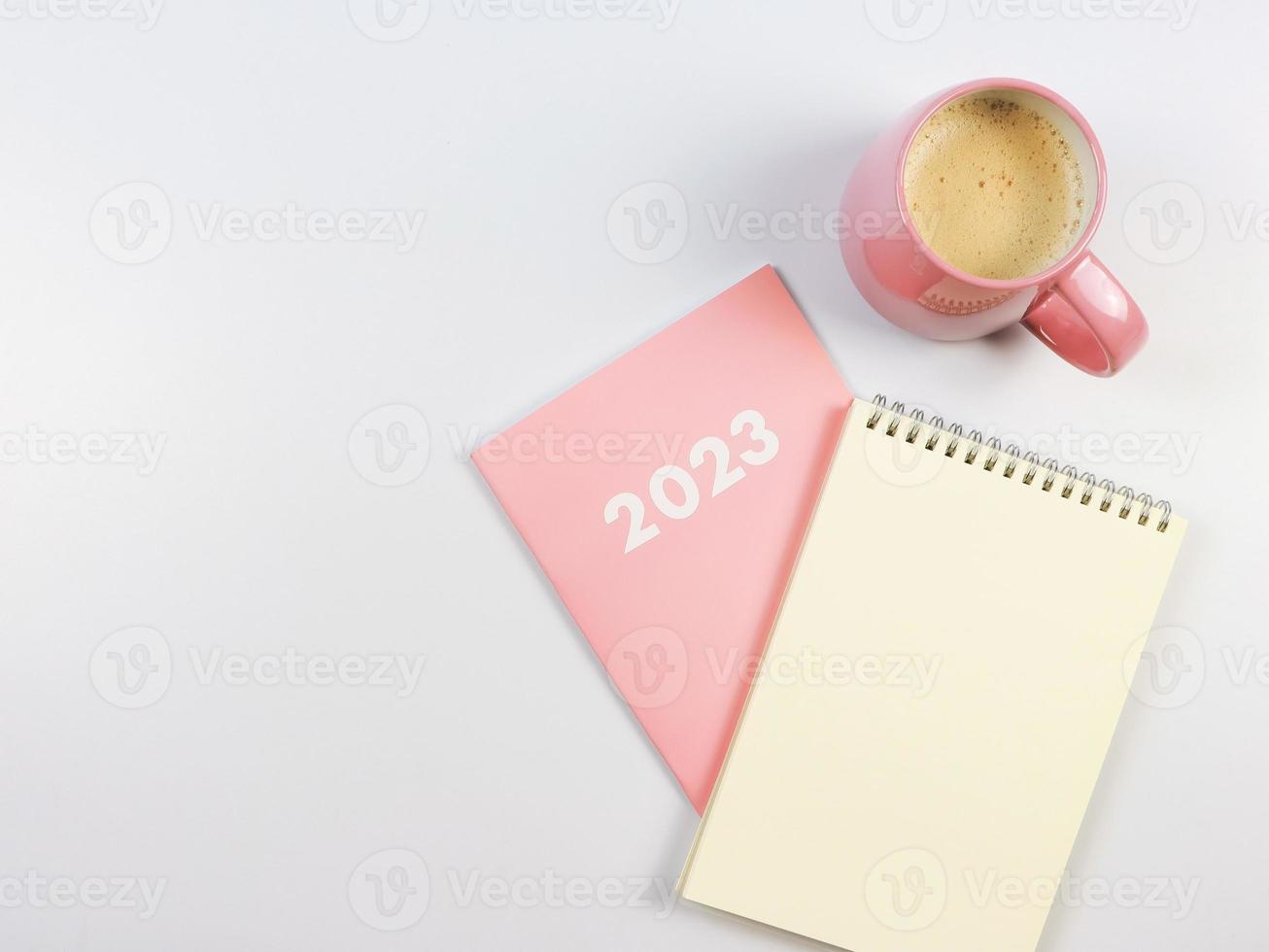 flat lay of blank paper note book on pink diary 2023 and pink cup of coffee on white background. photo