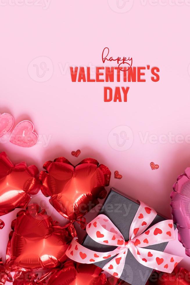 Happy Valentines Day text and gift box, candels and red heart shape baloons on pink background. Valentines Day greeting card vertical format photo