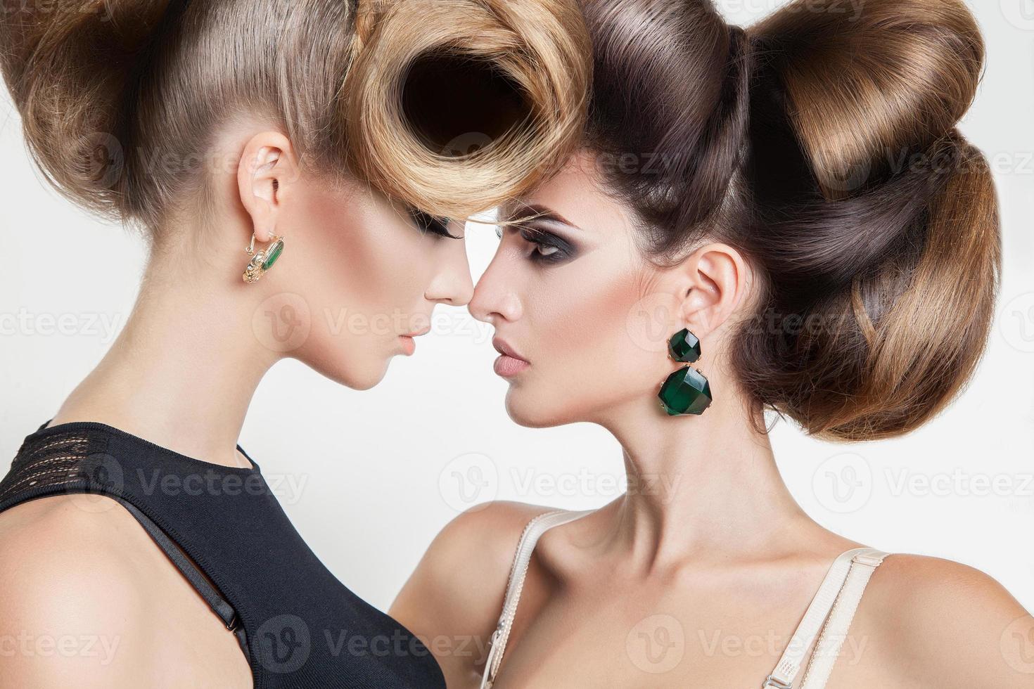 Portrait of two sexy women in studio with volume creative hairstyle looking at each others photo