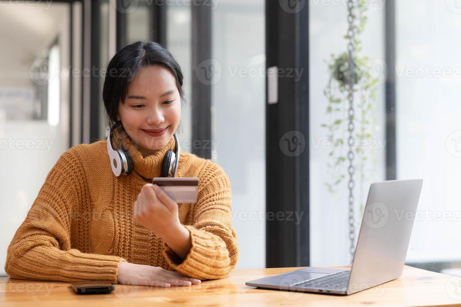 Attractive  Asian female sits at her desk, holding a smartphone and a credit card. close-up image. Online payment, credit card payment, mobile banking, online shopping, cashless society. photo