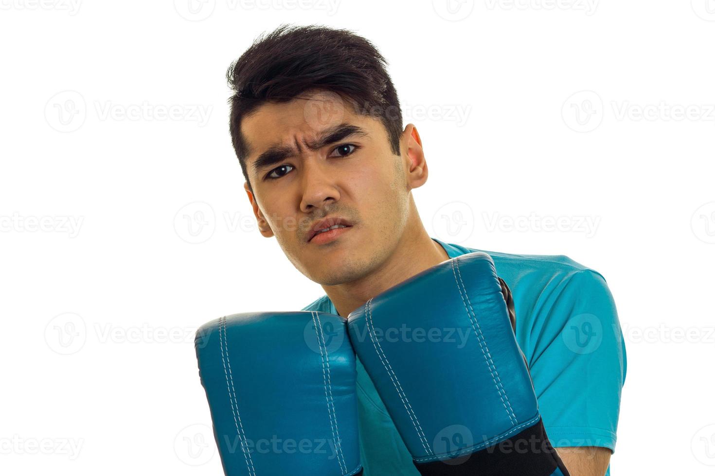 retrato de un deportista enojado con cabello oscuro practicando boxeo con guantes azules y uniforme aislado de fondo blanco foto