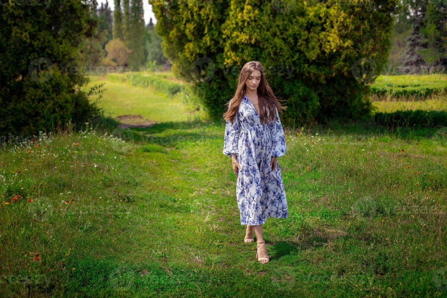 atractiva joven morena vestida con estampado de flores azules camina en el parque grren foto