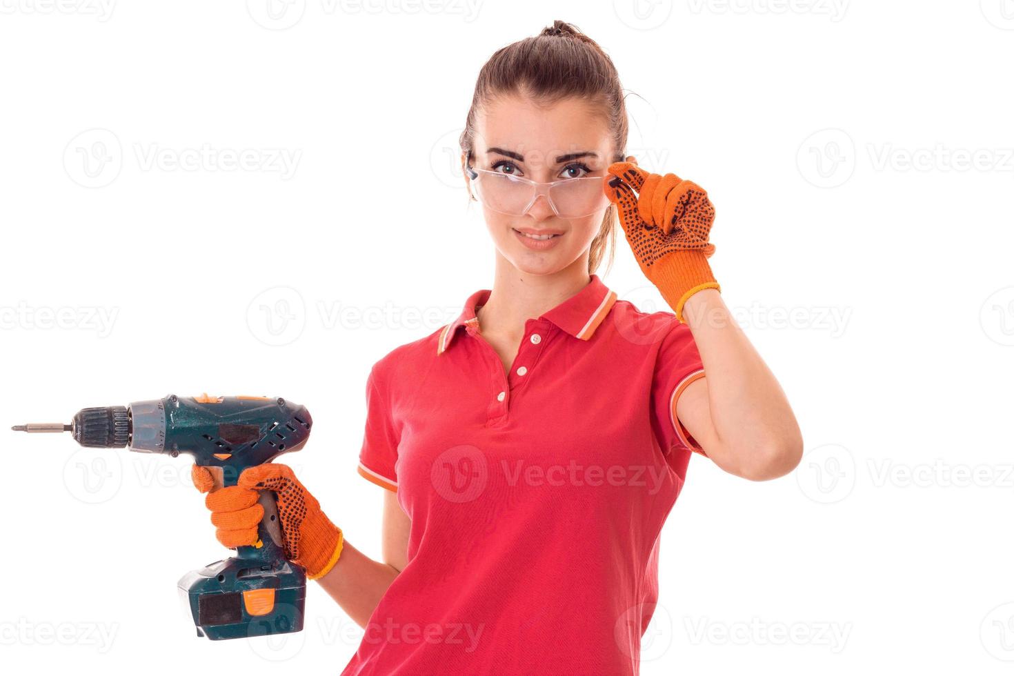 Una joven y encantadora constructora de uniforme con taladro en las manos hace una renovación aislada de fondo blanco foto