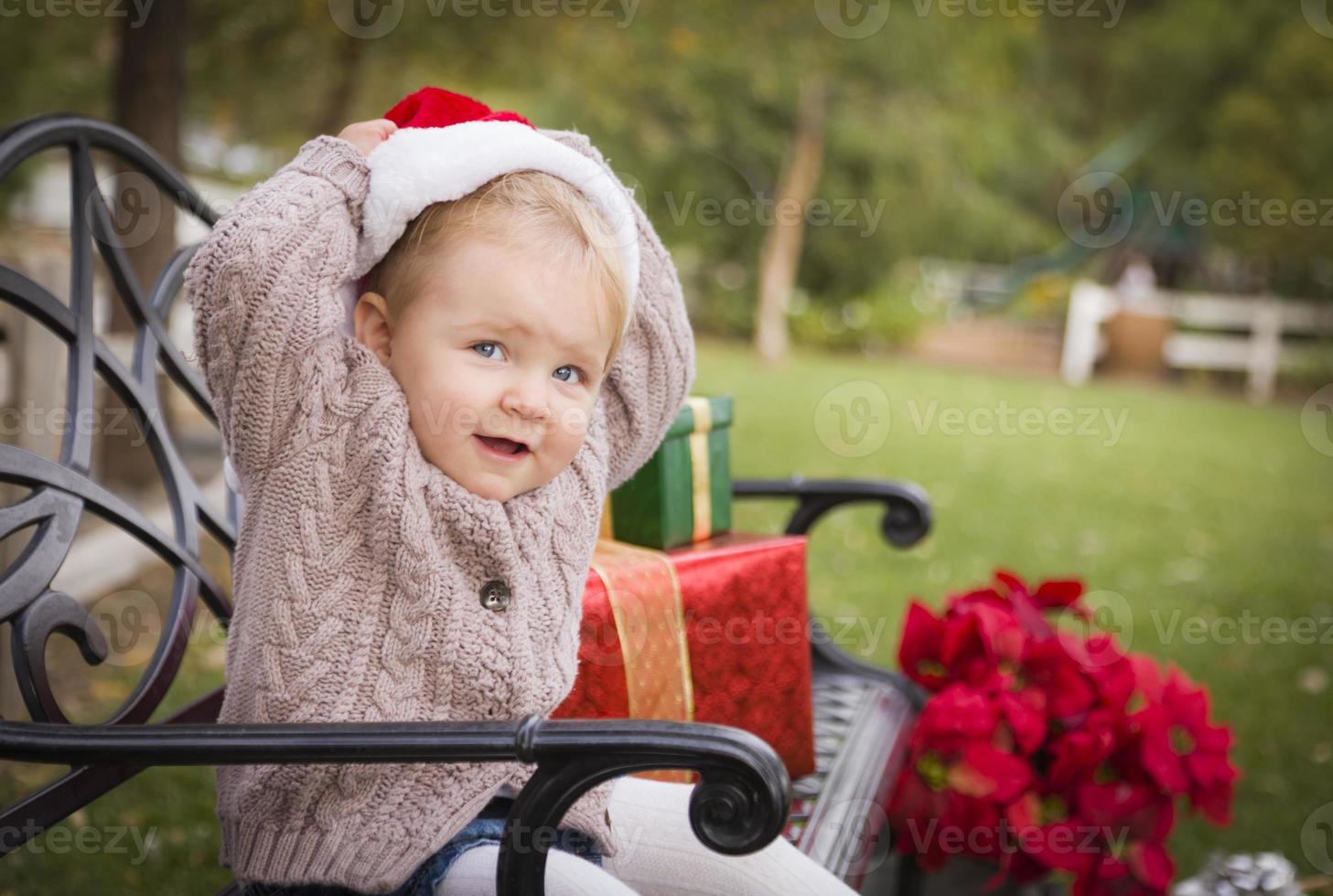 Young Child Wearing Santa Hat Sitting with Christmas Gifts Outside. photo