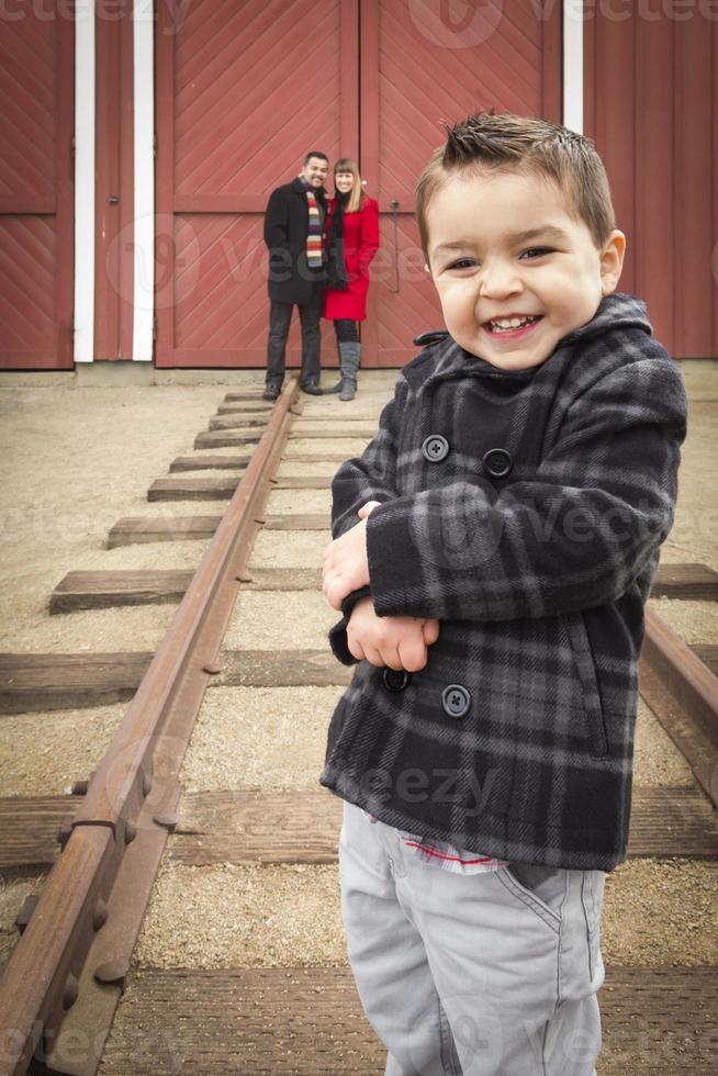 Mixed Race Boy at Train Depot with Parents Smiling Behind photo
