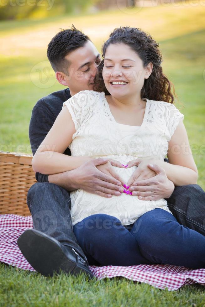 Pregnant Hispanic Couple Making Heart Shape with Hands on Belly photo