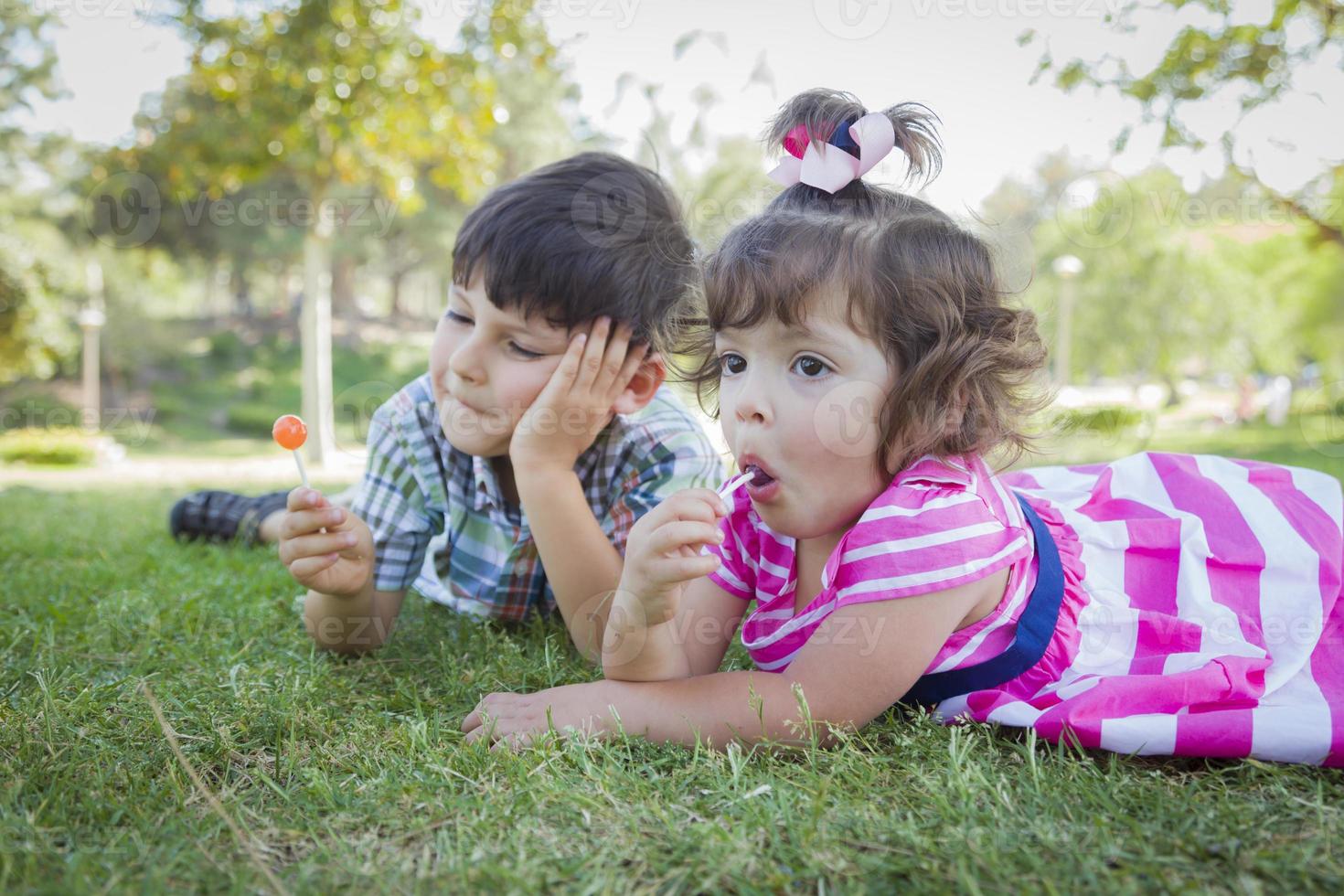 Young Brother and Baby Sister Enjoying Their Lollipops Outdoors photo