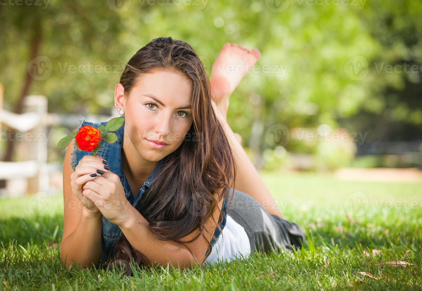 Attractive Mixed Race Girl Portrait Laying in Grass Outdoors with Flower. photo