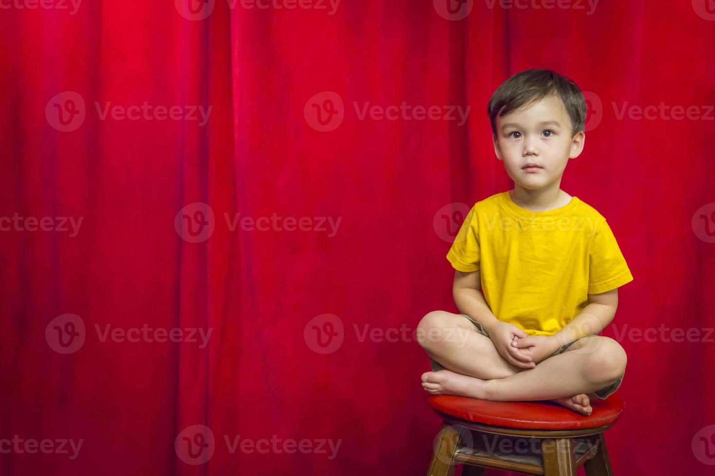 niño de raza mixta sentado en un taburete frente a la cortina foto