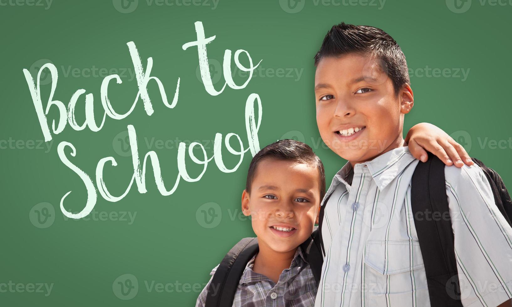 Hispanic Boys Wearing Backpacks In Front of Back To School Written On Chalk Board photo