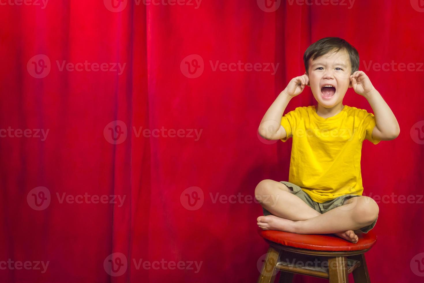 niño, dedos en los oídos en un taburete frente a la cortina foto