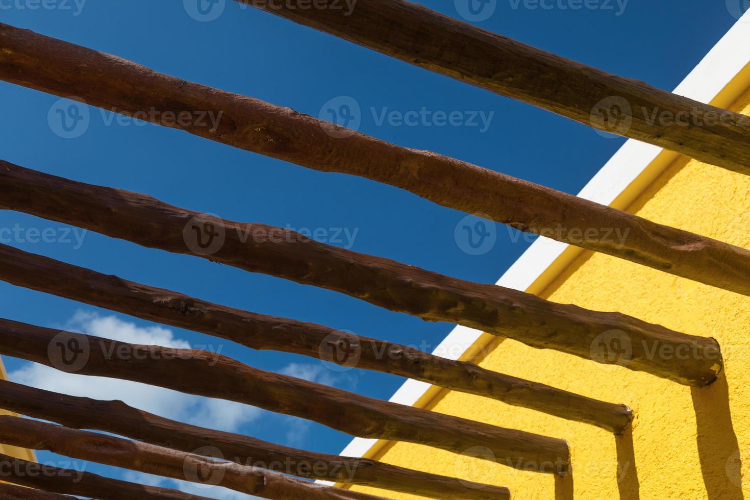 Abstract Wood Post Beams and Bright Yellow Wall Against Blue Sky photo