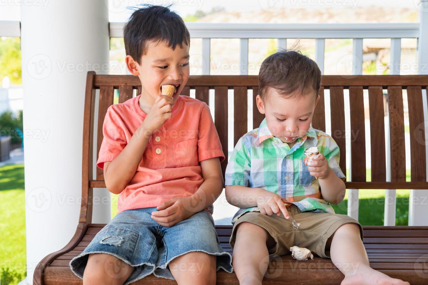 jóvenes hermanos chinos y caucásicos de raza mixta disfrutando de sus conos de helado foto