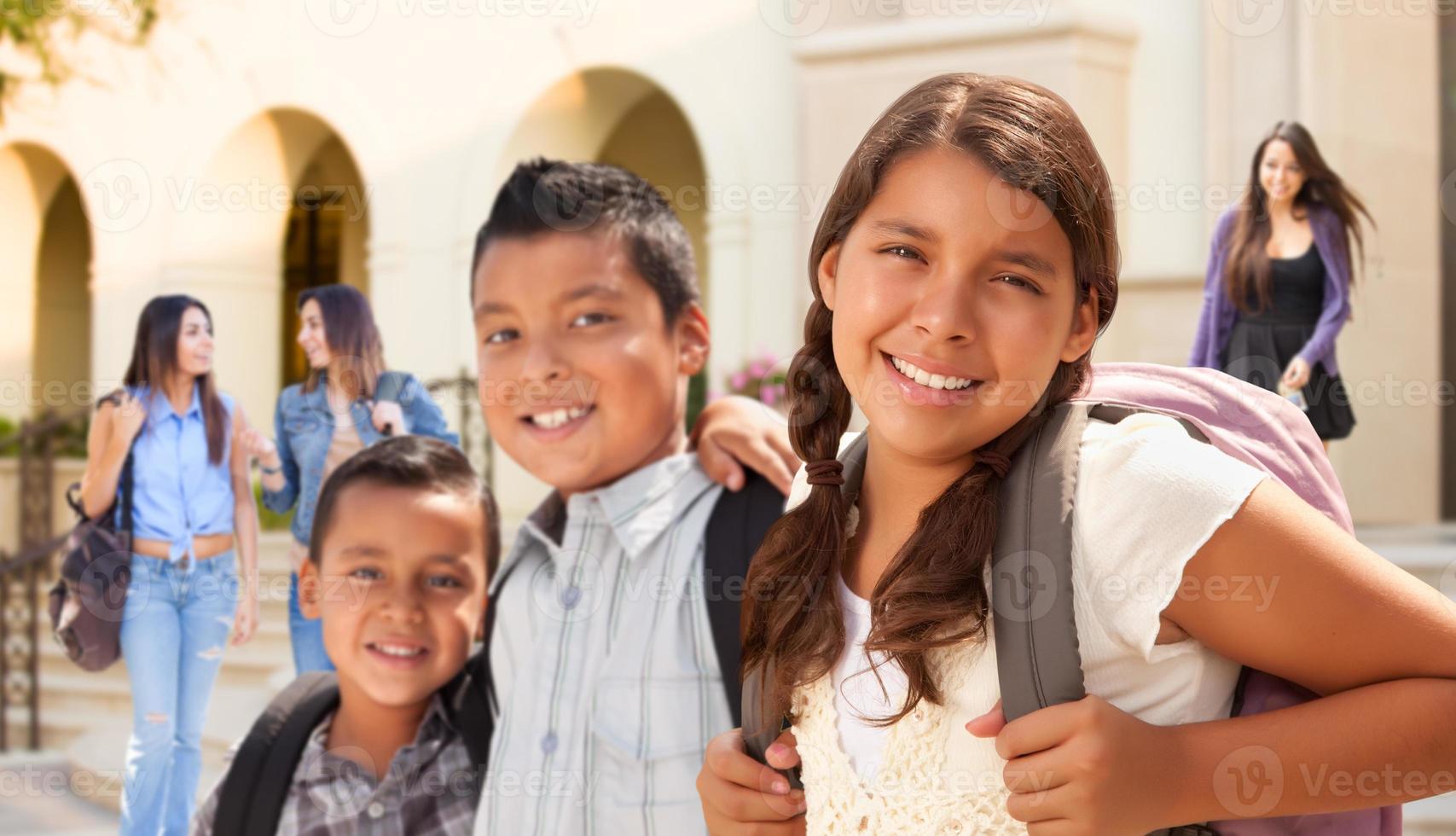 Young Hispanic Student Children Wearing Backpacks On School Campus photo