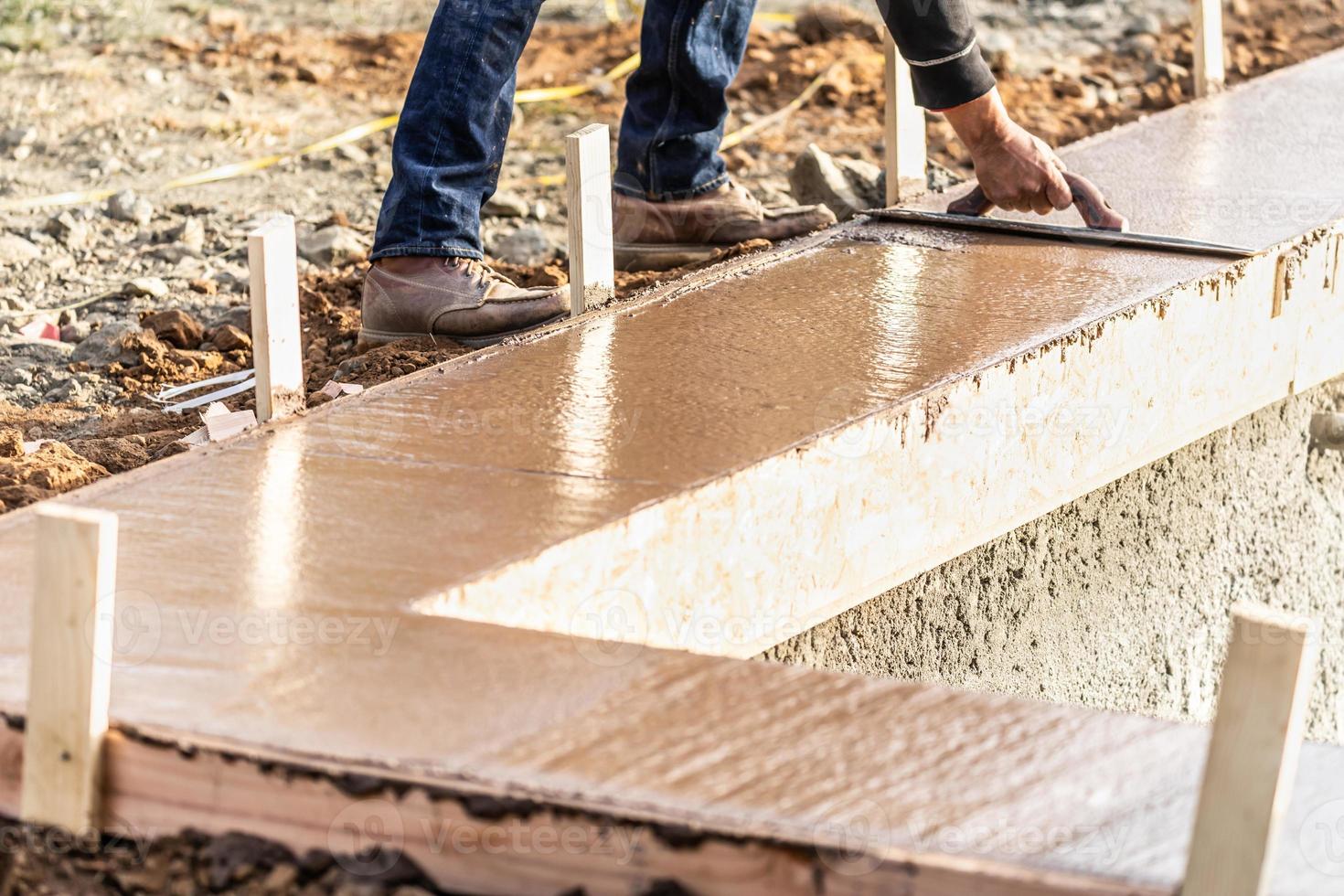 trabajador de la construcción usando paleta de madera en cemento húmedo formando para hacer frente a la nueva piscina foto