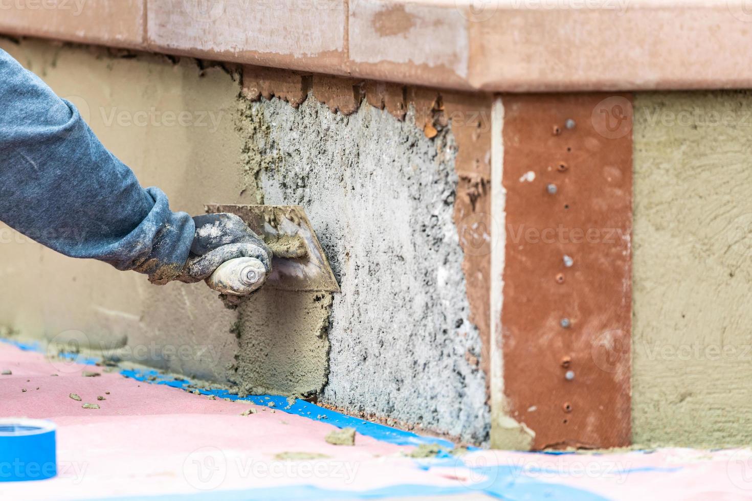 trabajador de baldosas aplicando cemento con paleta en el sitio de construcción de la piscina foto