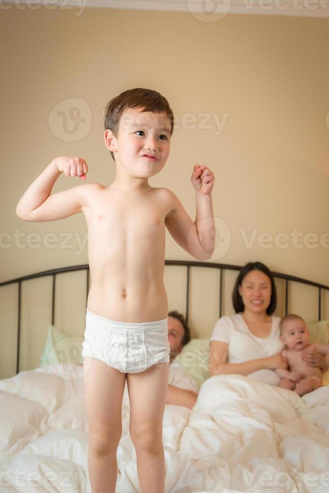 niño chino y caucásico de raza mixta saltando en la cama con su familia foto