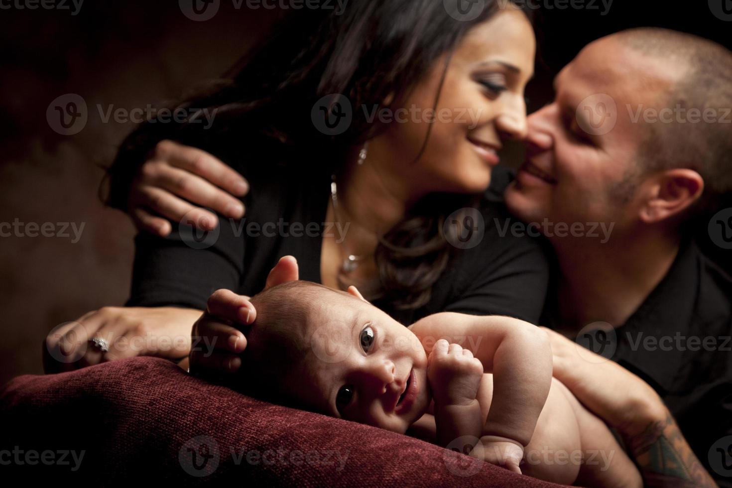 Una pareja de raza mixta mira amorosamente mientras el bebé se acuesta en la almohada foto