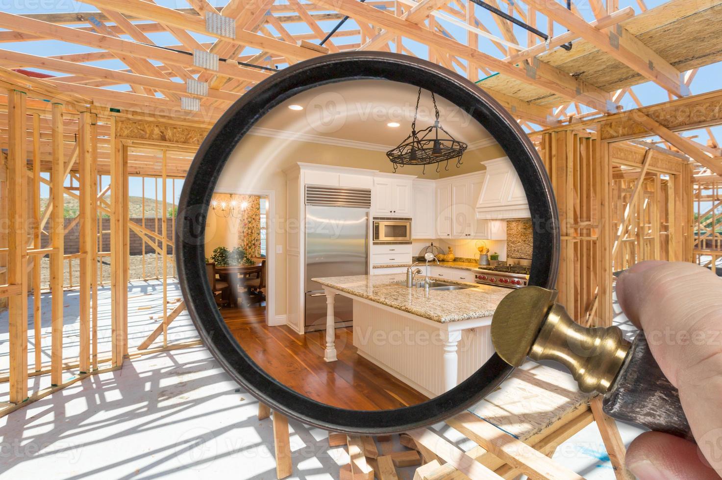 Hand Holding Magnifying Glass Revealing Finished Kitchen Build Over Construction Framing photo