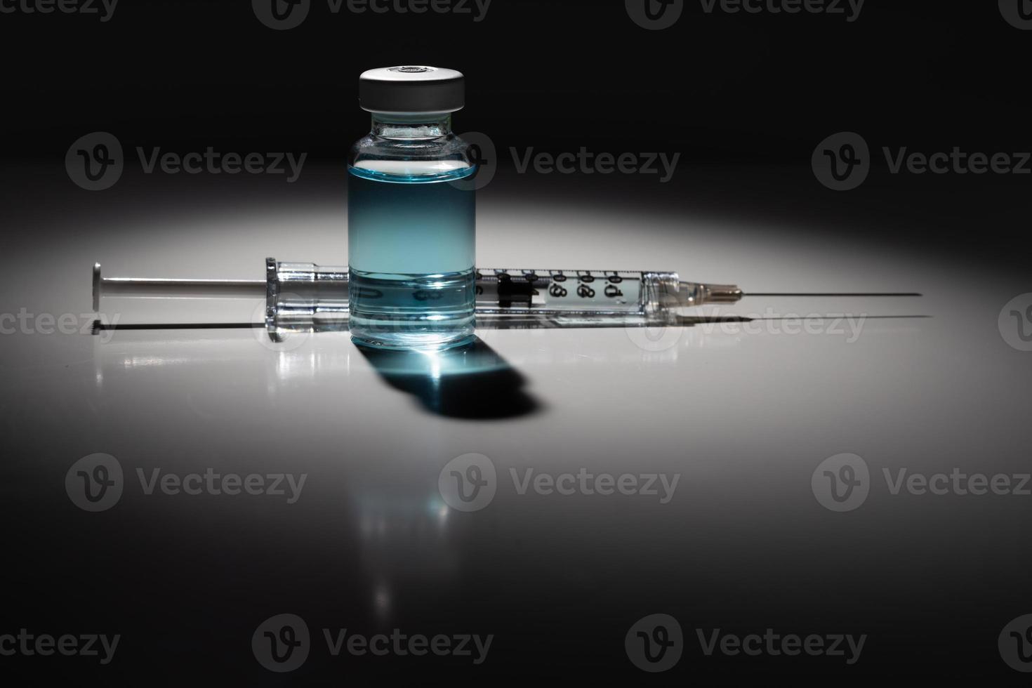 aguja de jeringa y vial de medicamento con punto químico azul claro iluminado sobre fondo reflectante foto